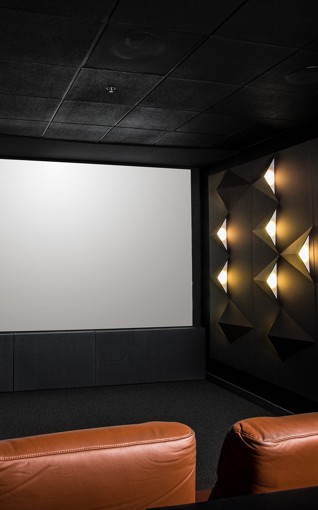 Portrait High-end home theater room facing large blank screen with brown leather chairs.