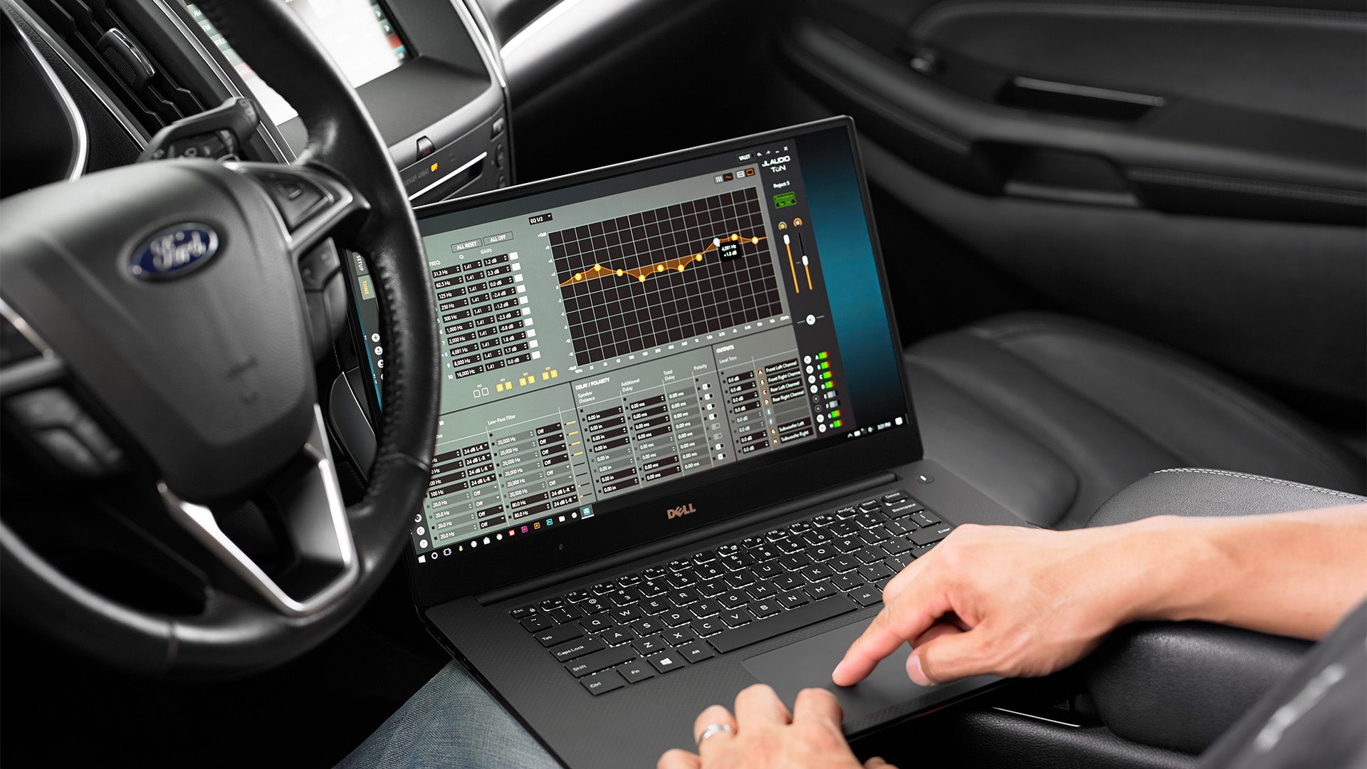 A man sitting in a ford vehicle using TuN software on a laptop to make audio frequencies adjustments.