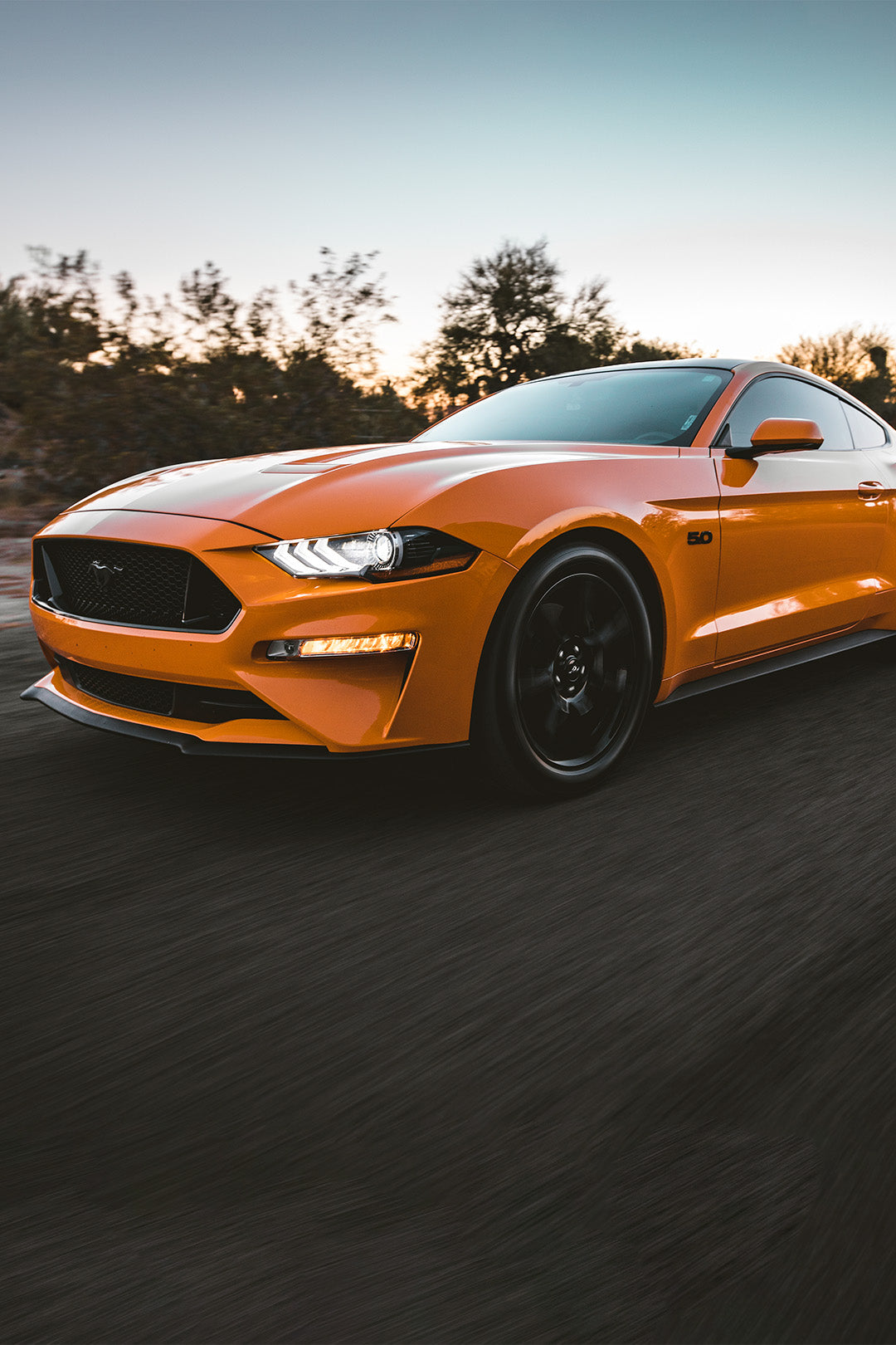 A ford mustang being driven on a road at sunset.