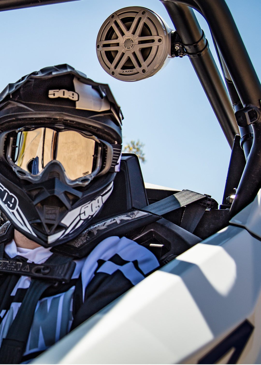 A powersports driver with helmet and gear sitting in a vehicle with install VeX audio system.