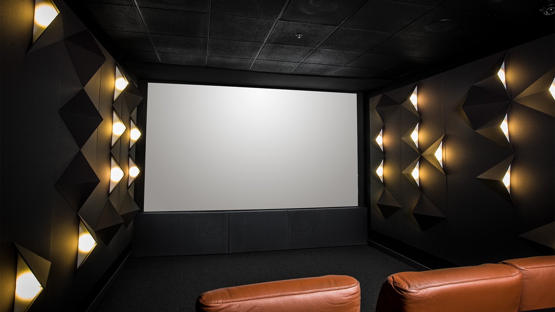High-end home theater room facing large blank screen with brown leather chairs.