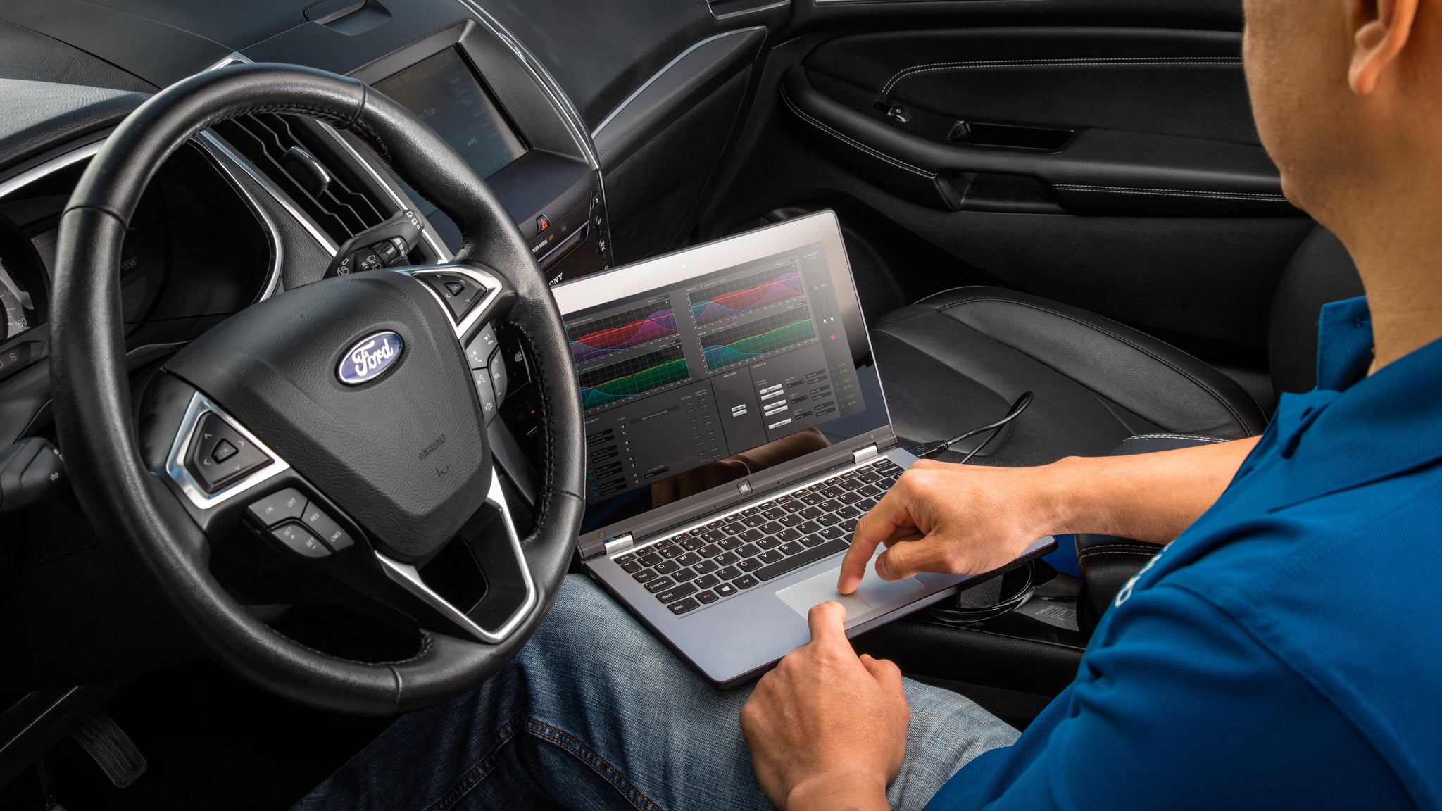 A technician using FiX EOM DSP integration with his laptop to adjust audio levels for a vehicle.