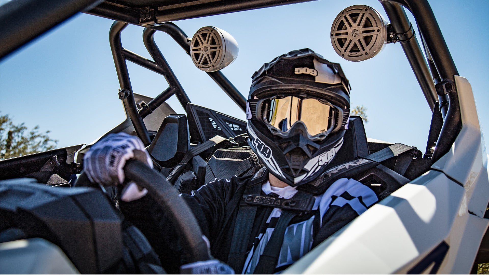 A powersports driver with helmet and gear sitting in a vehicle with install VeX audio system.